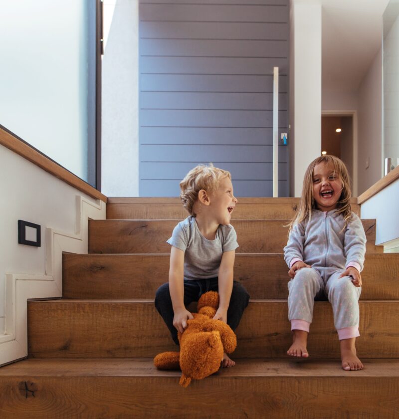 Lachende Kinder auf breiten Holzstufen zeigen, wie wichtig Sicherheit beim Treppen planen sind